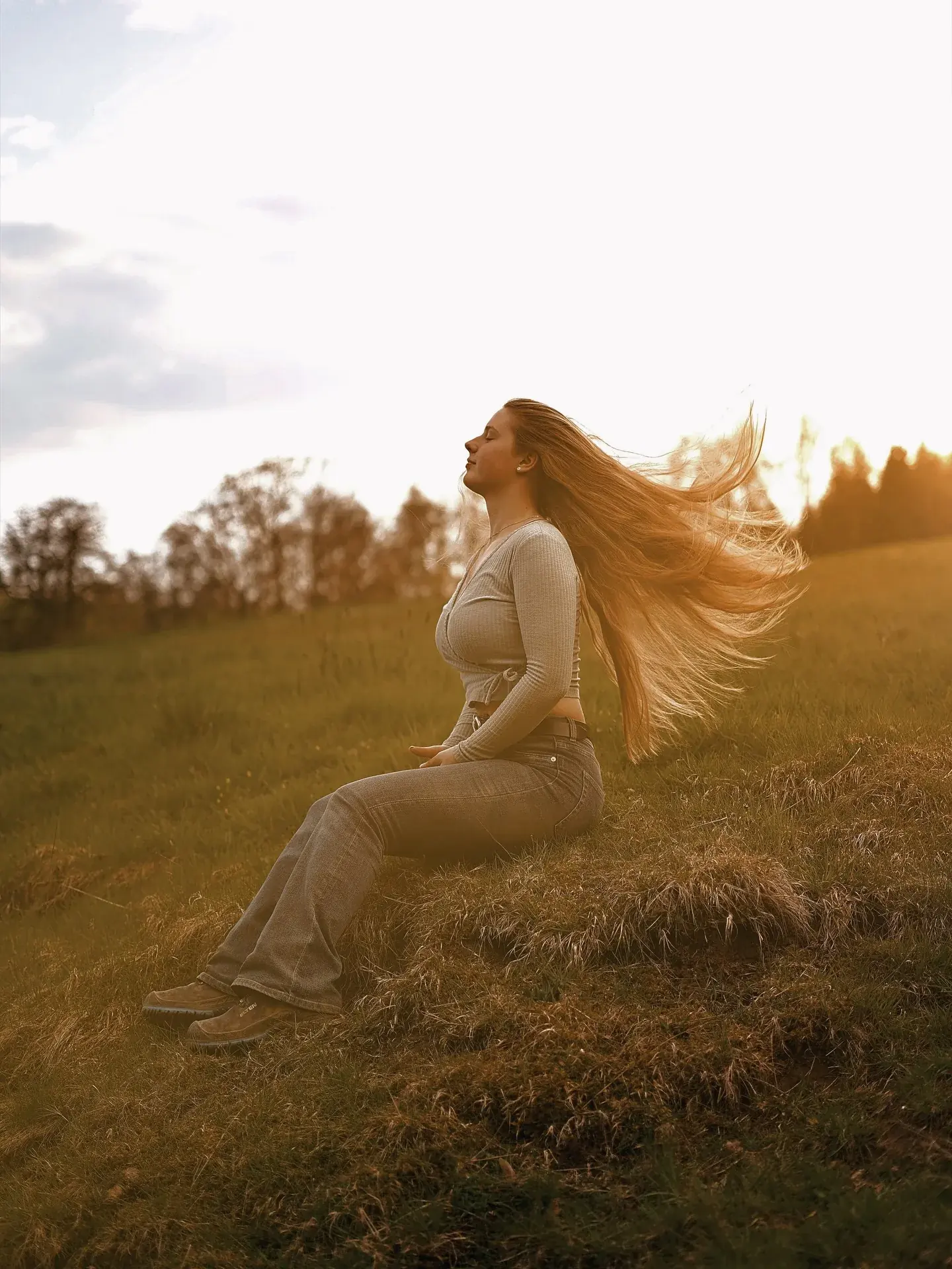 Frau sitzt im Feld bei Sonnenuntergang, Haare im Wind