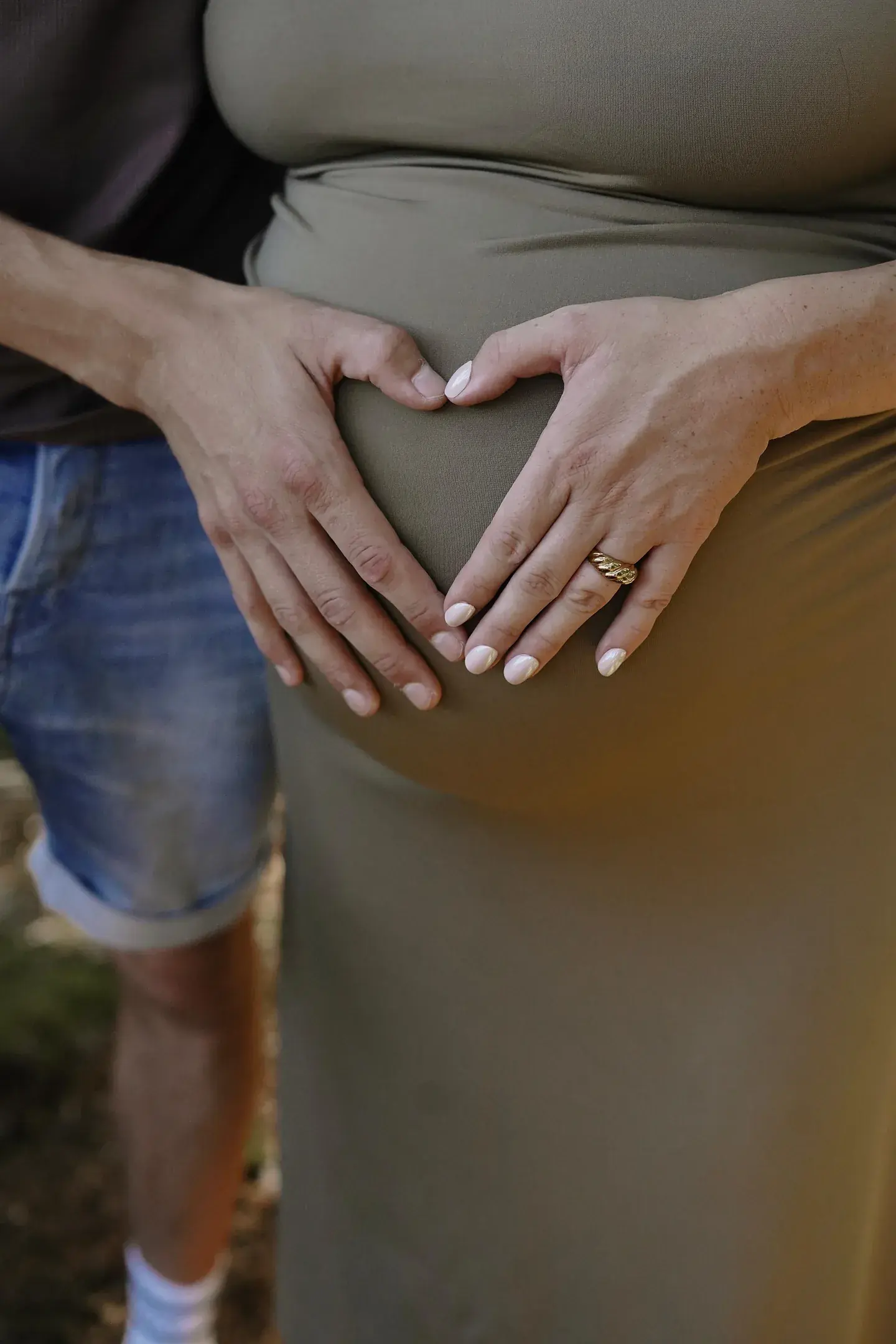 Hände formen ein Herz auf einem Babybauch